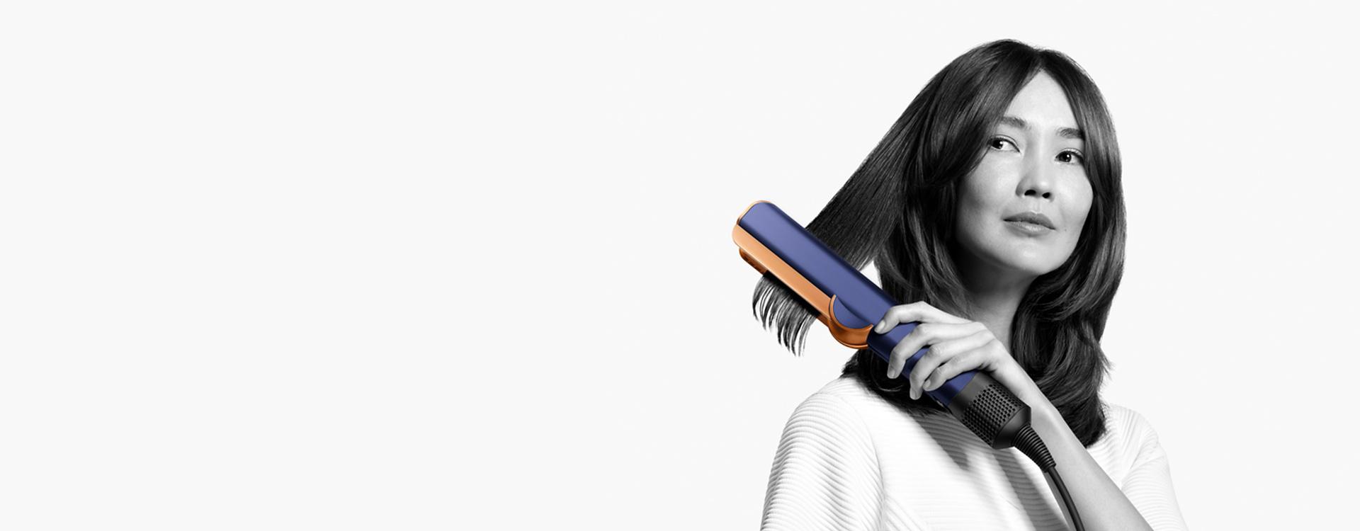 Woman using a Dyson Airstrait straightener to dry and straighten a tress of her hair.