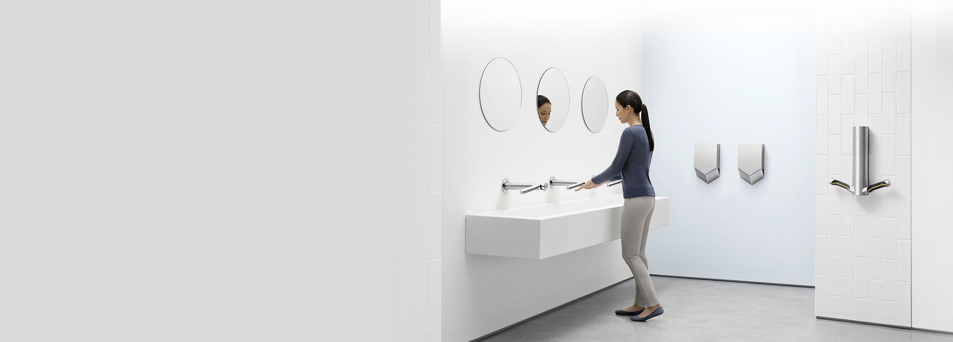 אישה בחדר שירותים מוקפת במכשירי Dyson Airblade שונים