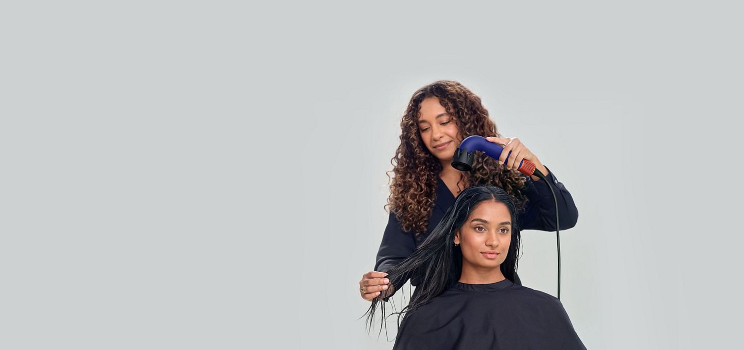 Coiffeuse séchant les cheveux de sa cliente avec le sèche-cheveux Dyson Supersonic r Professionnel muni du concentrateur Pro et de la brosse à rouleau ventilé.