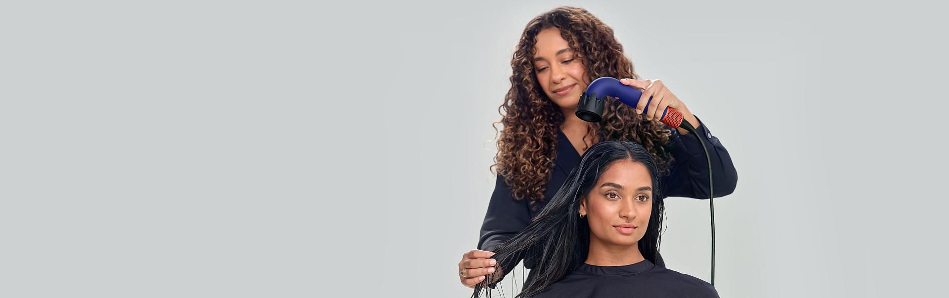 Stylist drying hair with the Dyson Supersonic r Professional hair dryer with the Pro concentrator attachment and Vented barrel brush.