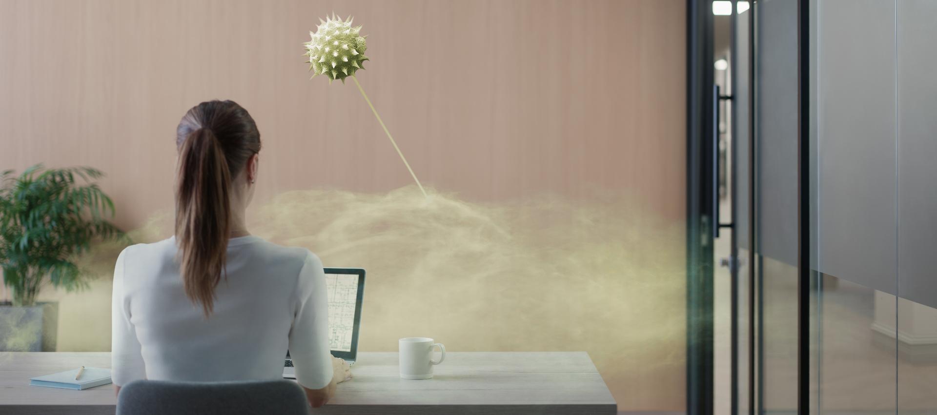 A woman sitting at a desk in an office meeting room. A microscopic image shows pollution in the air.