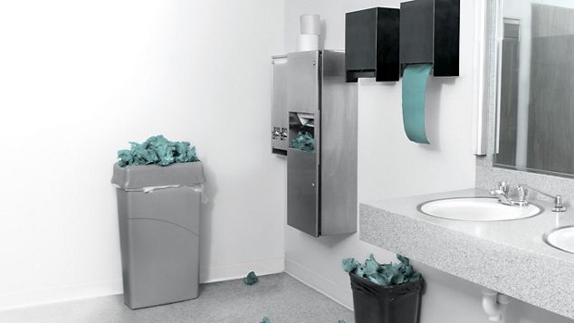 A public bathroom with paper towel dispensers and trash cans.