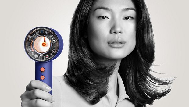 Model removing flyaways with the Dyson Supersonic hair dryer and Flyaway attachment.