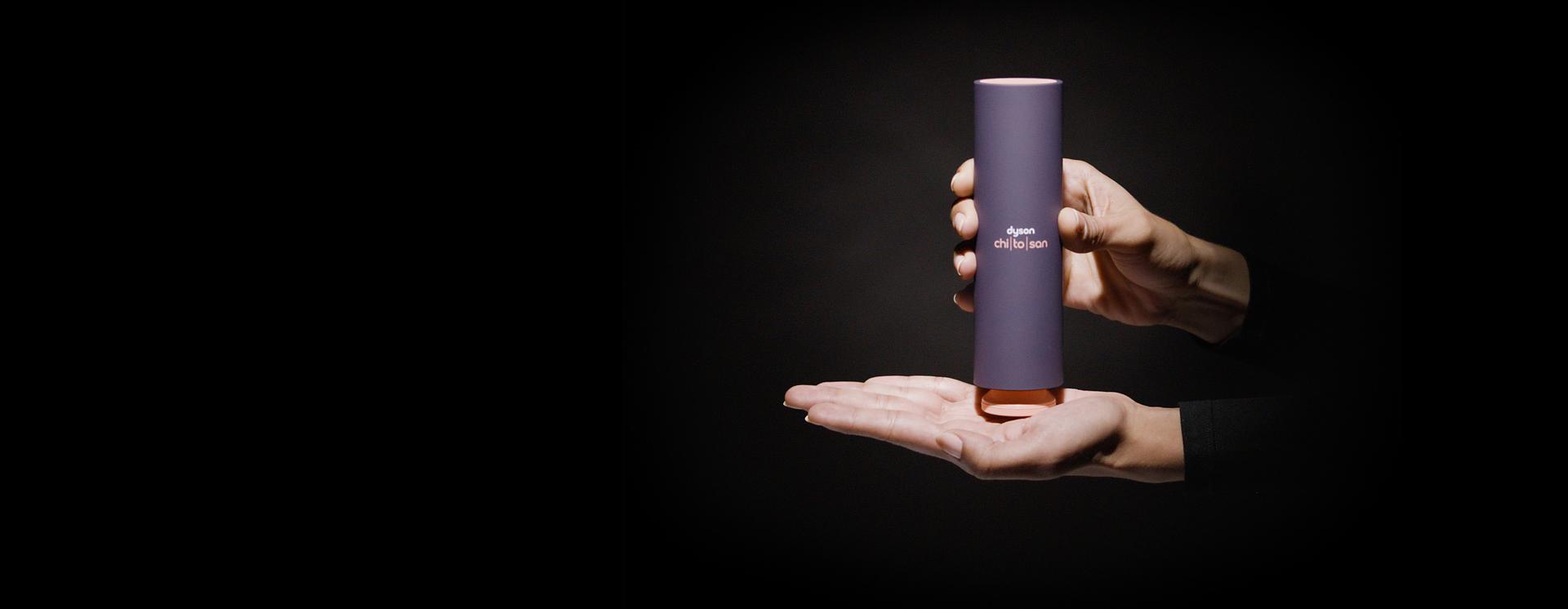 A hand holds a bottle of Dyson Chitosan, with the pump positioned mid-palm