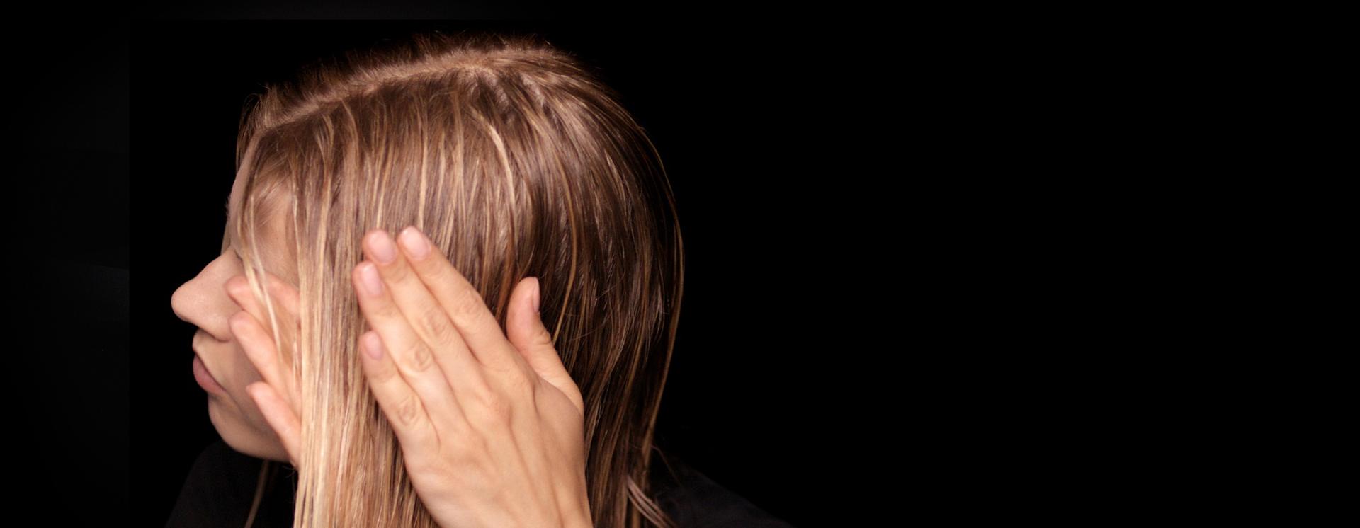 عارِضة شعرها طويل ورطب تَستخدم يديها لتنعيم المستحضر على امتداد طول الشعر