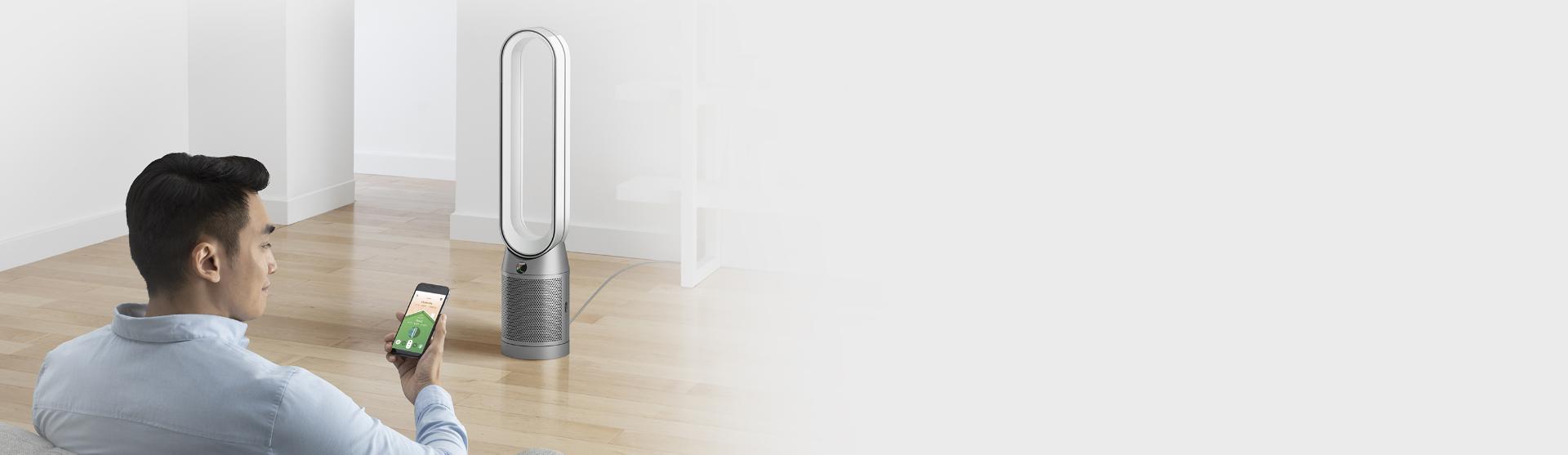 Mężczyzna siedzący przed oczyszczaczem firmy Dyson, korzystając z aplikacji Dyson Link w telefonie