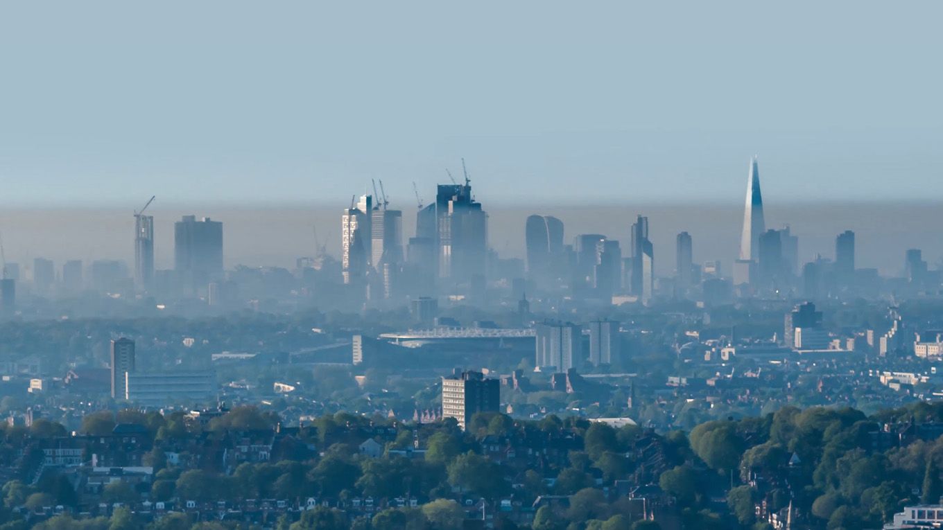 A cityscape with smoke above a treeline.