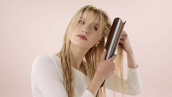 A blonde model uses the Root drying mode on the Dyson Airstrait to add volume to her hair.