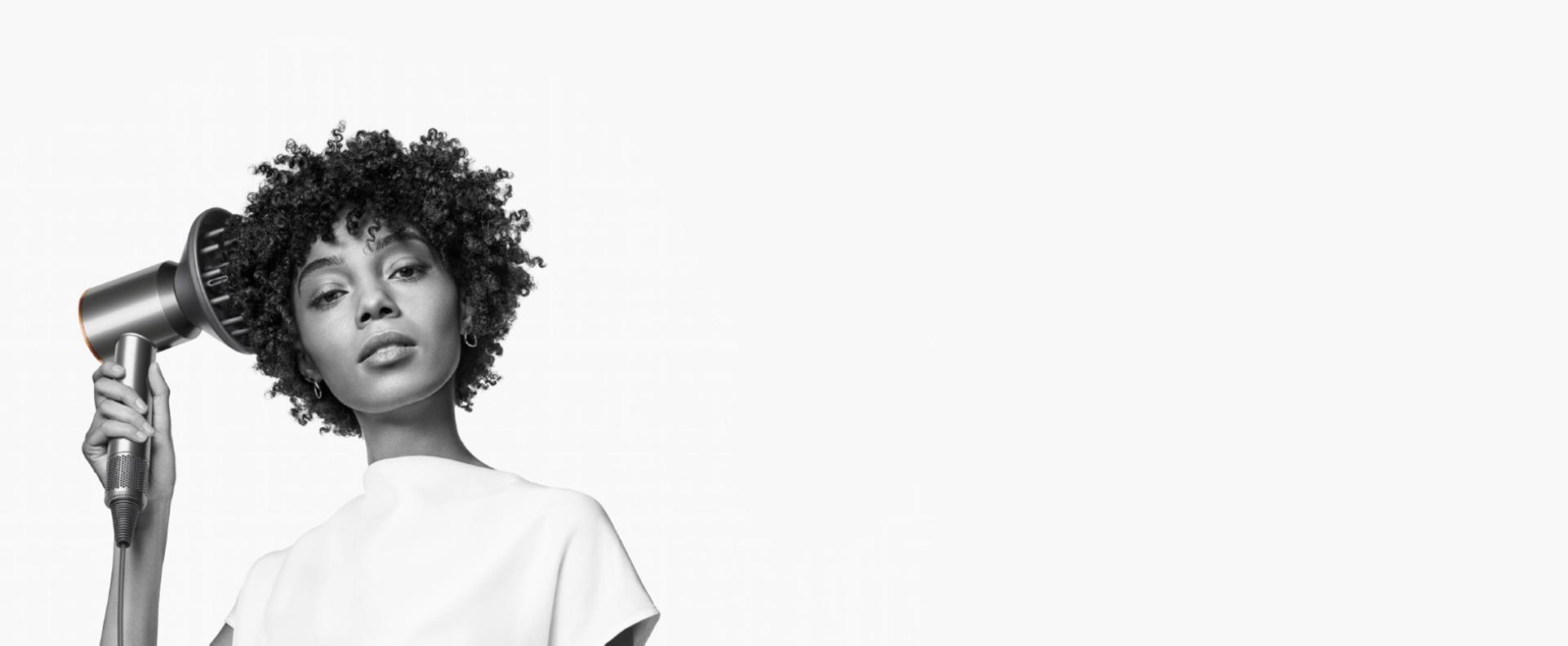 سيدة شعرها من النوع الرابع تَستخدم مجفف الشعر Dyson Supersonic