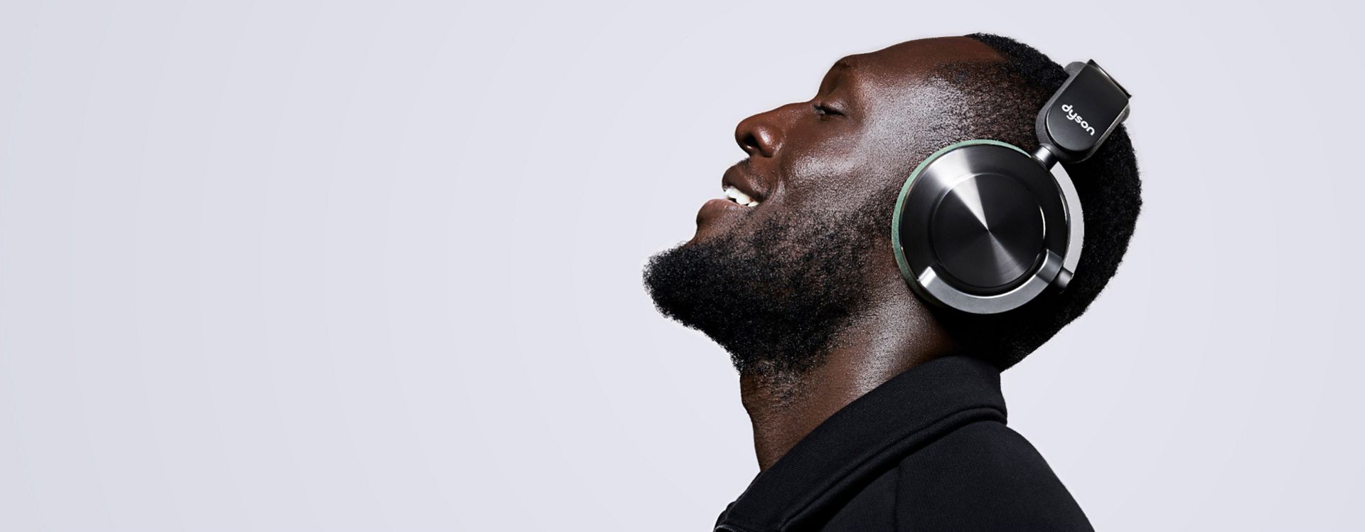 Stormzy nosi słuchawki Dyson OnTrac z zewnętrznymi nakładkami w kolorze czarny nikiel CNC i nausznikami w kolorze khaki.