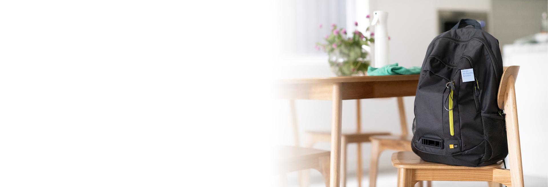 A black backpack, containing Dyson air quality monitoring technology, resting on a wooden kitchen chair.