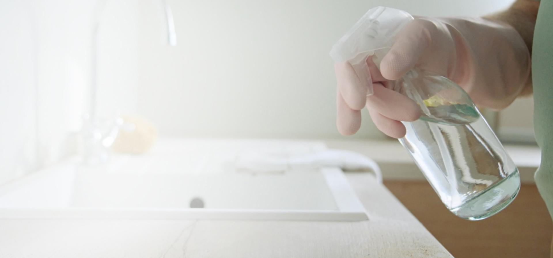 A gloved hand spraying a cleaning product onto a kitchen sink area.