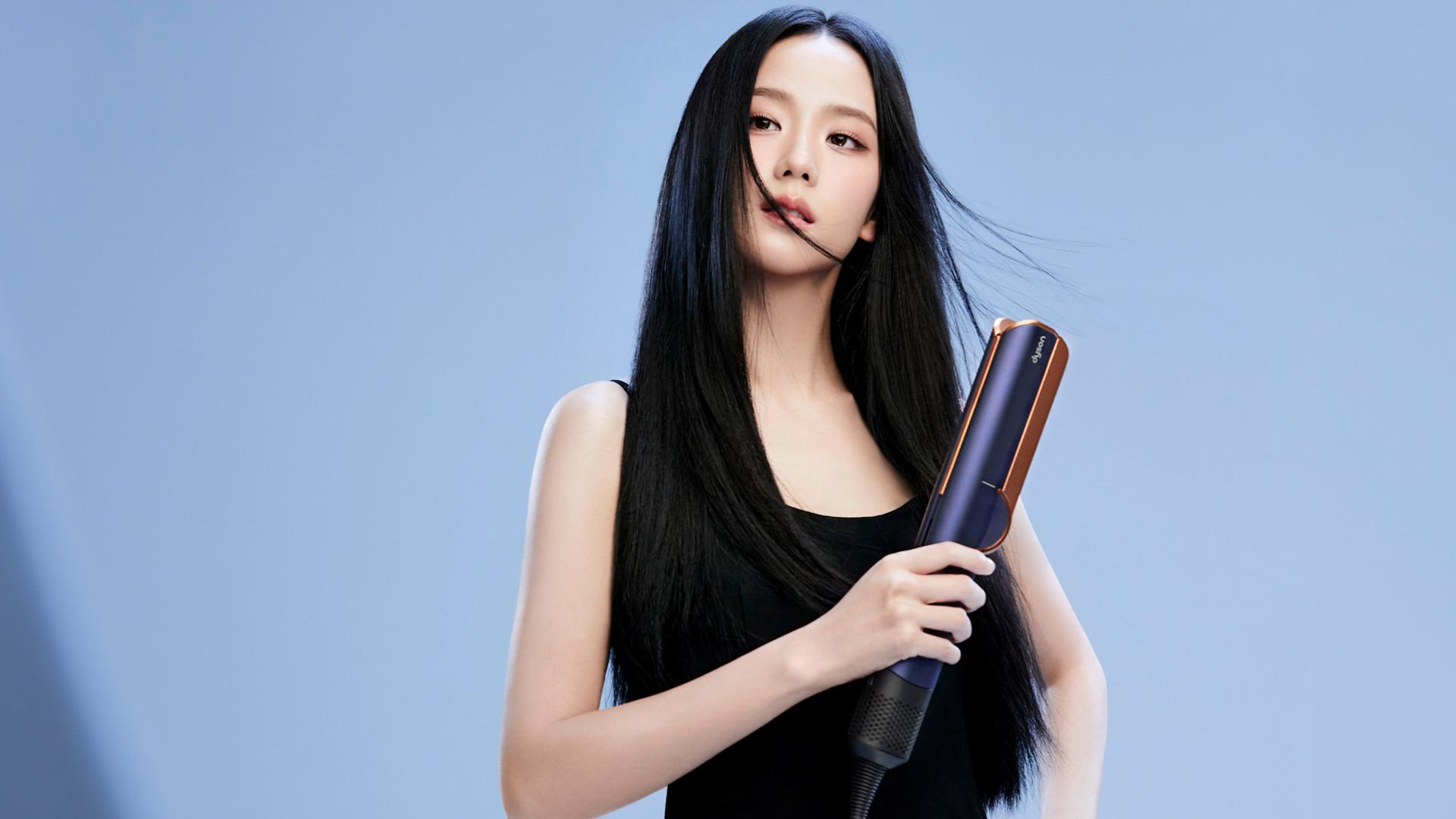 JISOO using a Dyson Airstrait straightener to dry and straighten a tress of her hair.