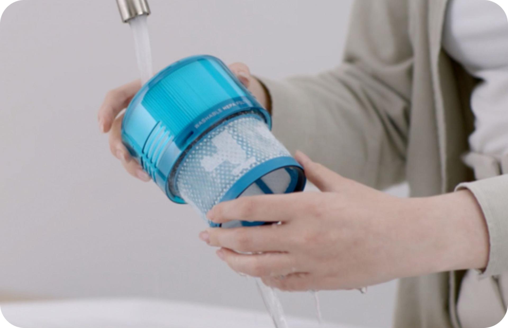 A close-up of a person washing a vacuum filter under a running tap
