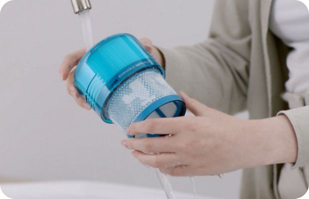 A close-up of a person washing a vacuum filter under a running tap