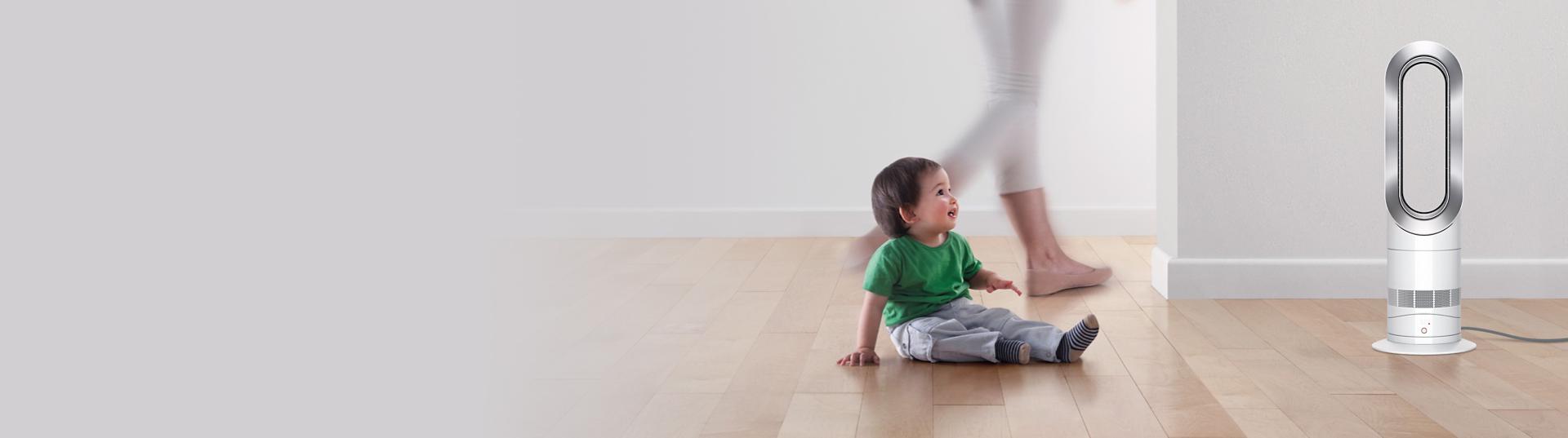 A small child sits safely next to a Dyson Hot+Cool Jet Focus fan heater while their parent walks behind.