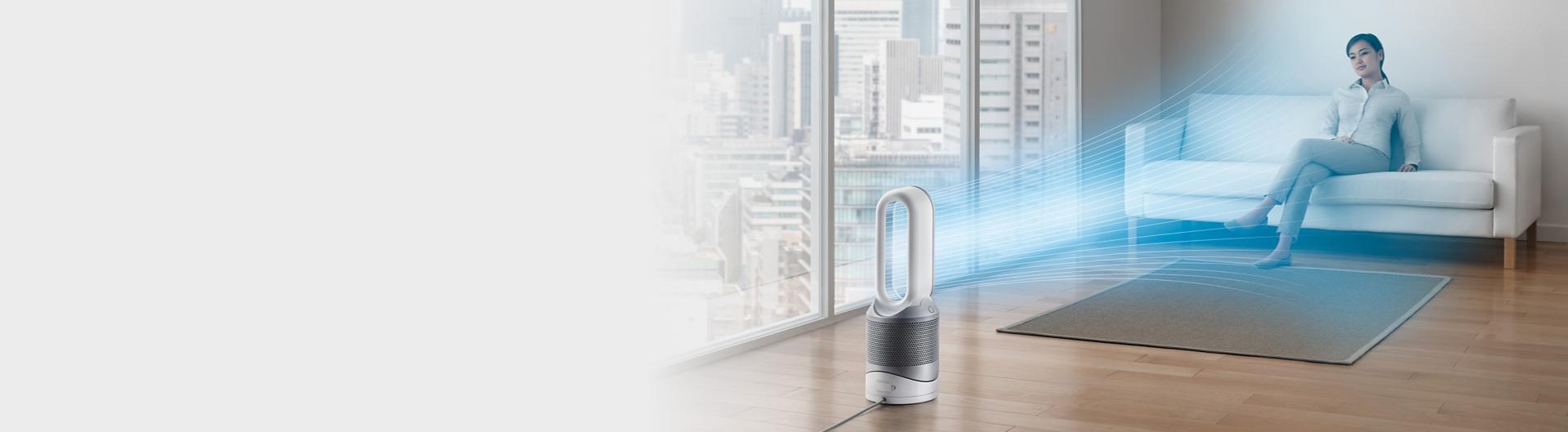 Dyson Pure Hot+Cool purifying fan heater purifying the air and cooling a woman on a sofa.