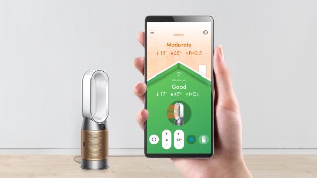 A hand holding a smartphone showing the air quality screen, with the Dyson Purifier Hot+Cool Formaldehyde.
