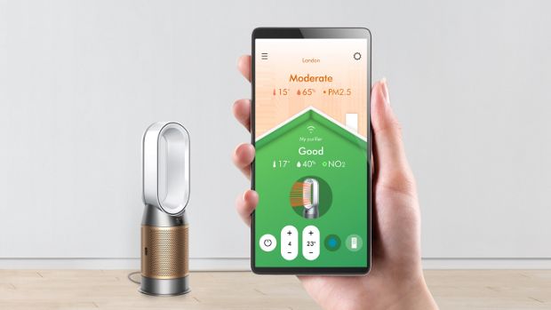 A hand holding a smartphone showing the air quality screen, with the Dyson Purifier Hot+Cool Formaldehyde.