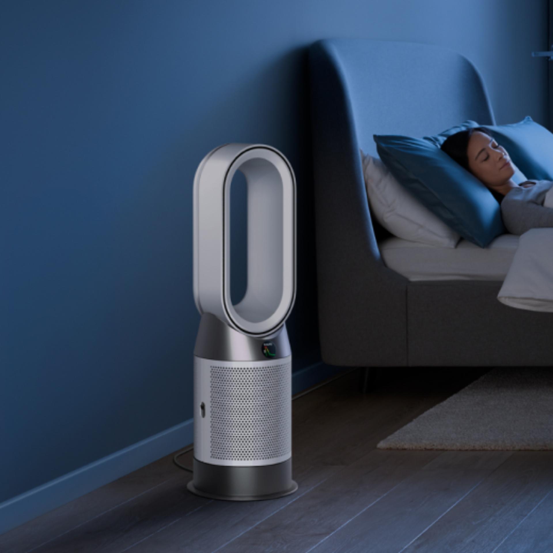 A Dyson Purifier Hot+Cool Gen1 purifying fan heater purifies the air next to a sleeping person.