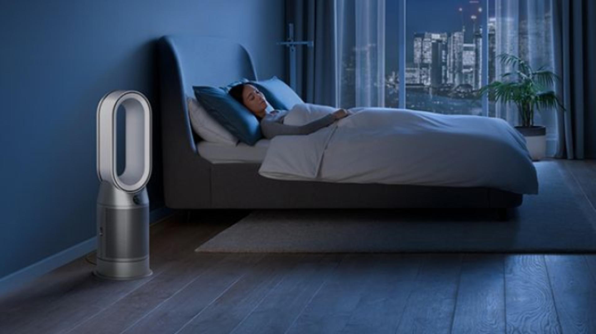 The Dyson Purifier Humidify+Cool Autoreact in a dark bedroom at night as a woman sleeps in her bed.