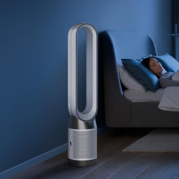 A Dyson Purifier Cool Gen1 TP10 purifying fan operates next to a person asleep in a bed.