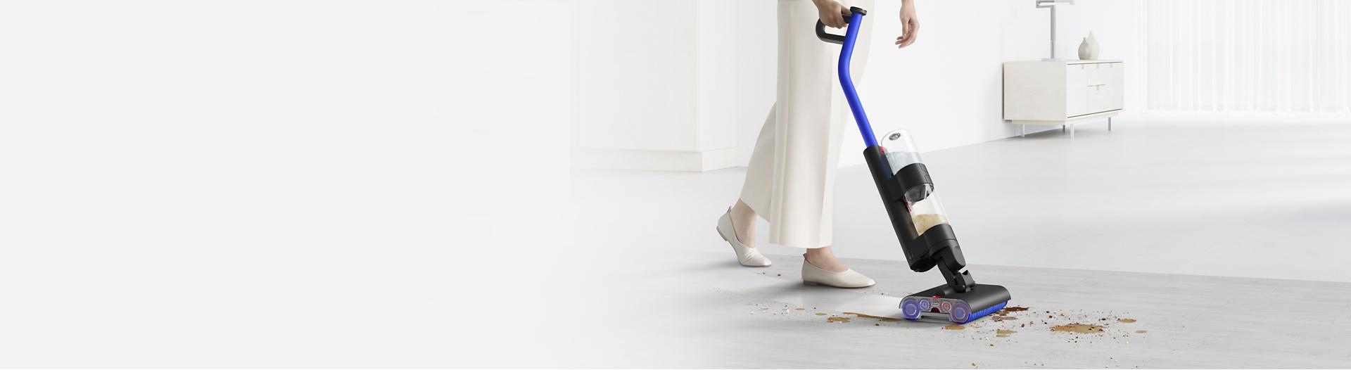 A woman cleans spills and debris from hard floor with the Dyson Wash G1 wet floor cleaner.