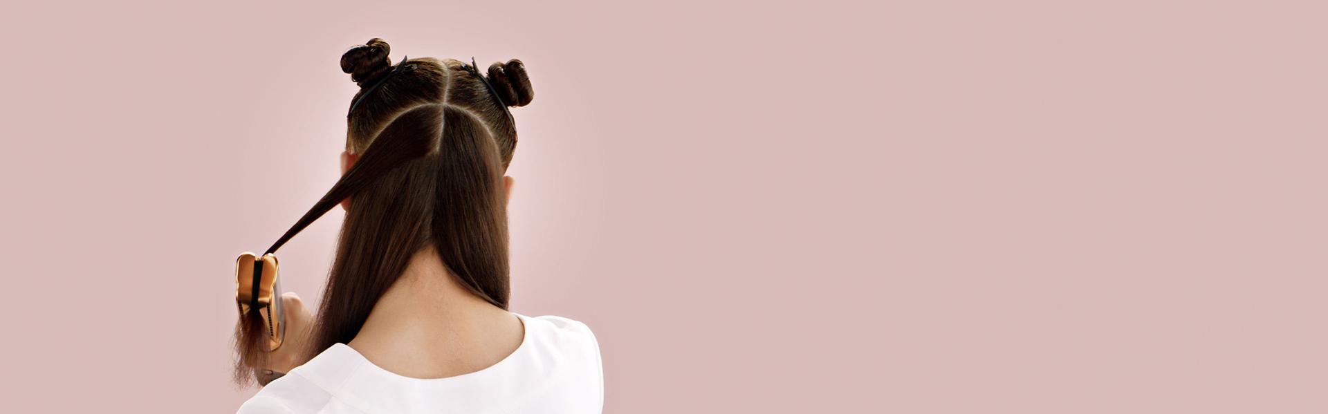 عارِضة شعرها بني طويل تُملِّس شعرها على طبقات باستخدام جهاز تمليس الشعر Dyson Airstrait.