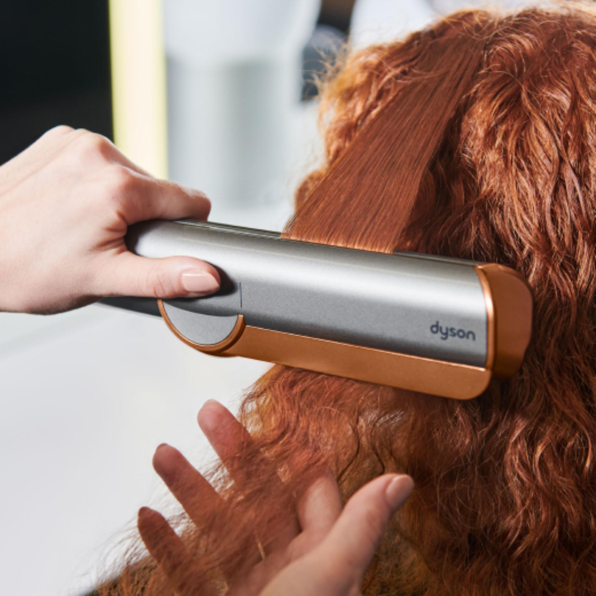 Close-up of the Dyson Airstrait straightener straightening long black hair.