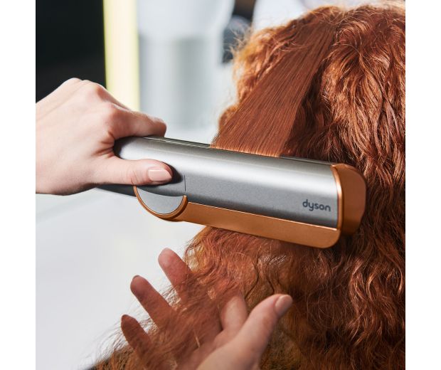 Zbliżenie prostownicy Dyson Airstrait prostującej długie, czarne włosy.