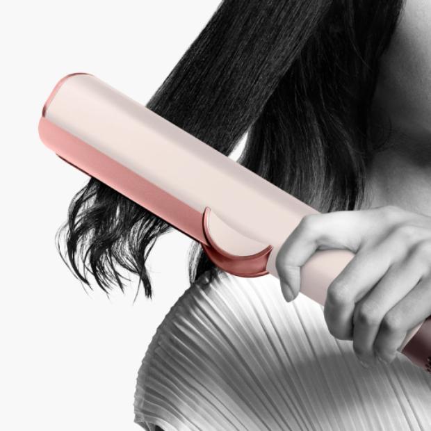 Close-up of the Dyson Airstrait straightener straightening long black hair.