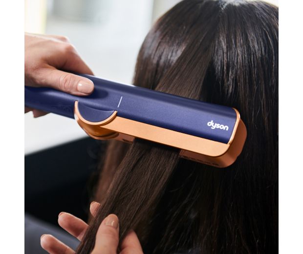 Close-up of the Dyson Airstrait straightener straightening long black hair.