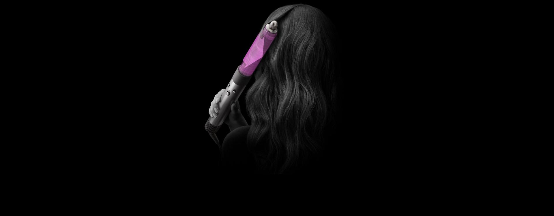 صورة مُقرَّبة لرأس سيدة من الخلف بينما تقوم بتجعيد شعرها باستخدام مجفف ومصفّف الشعر Dyson Airwrap متعدد الوظائف