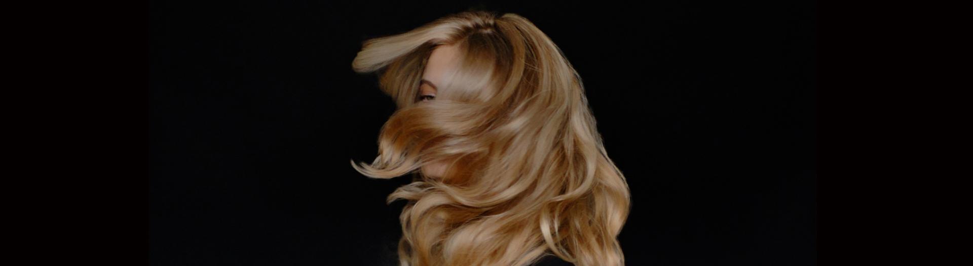 A blonde, long-haired model, flicks her hair over her shoulder.