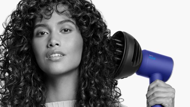 Close up of a woman adding volume to her curly hair with the Dyson Wave+Curl diffuser