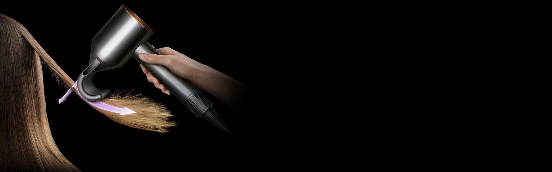 A woman hides flyaways in long brown hair using the Dyson Supersonic hair dryer and Flyaway attachment.