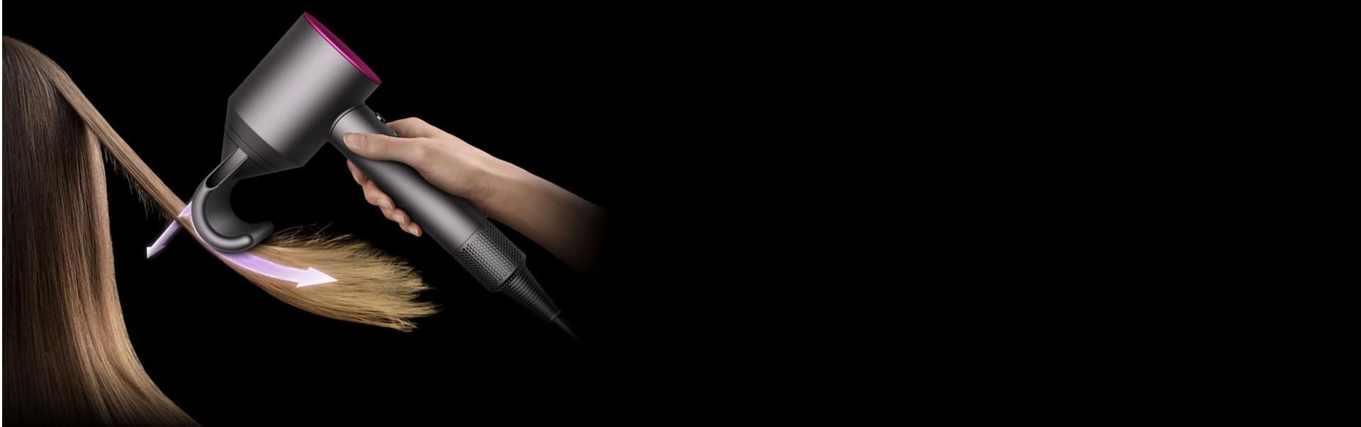 Dyson Supersonic saç kurutma makinesi ve Flyaway başlık kullanarak saçlarındaki elektriklenmeyi gideren, uzun kahverengi saçlı bir kadın.