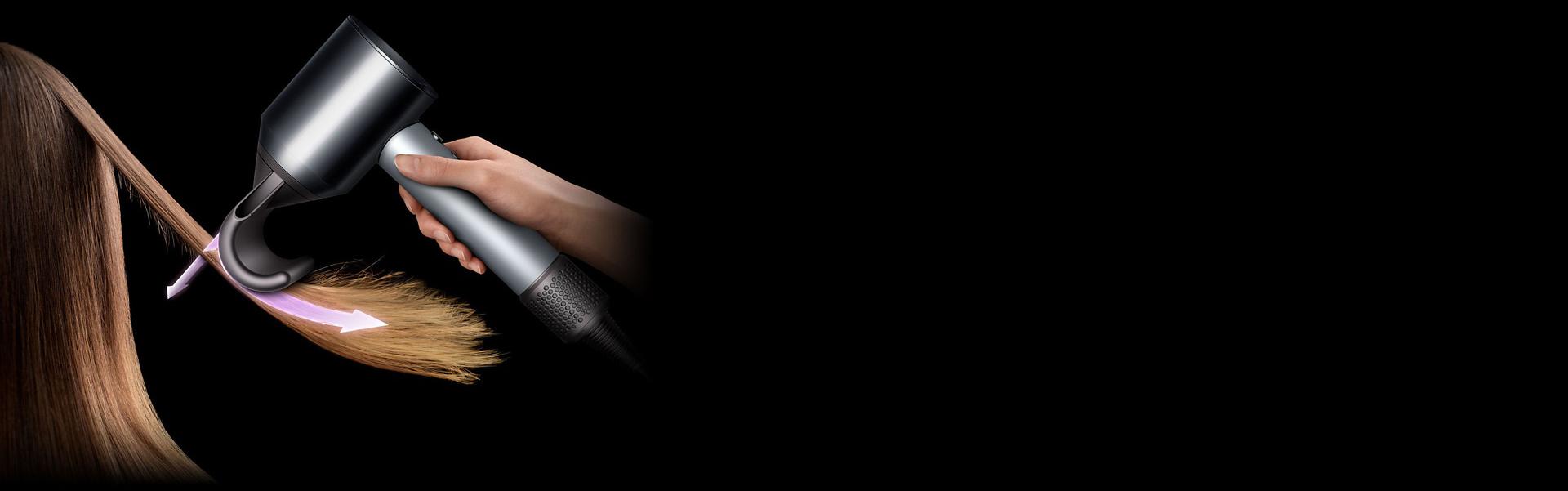 Kobieta ukrywa puszące się kosmyki na długich ciemnych włosach za pomocą suszarki Dyson Supersonic i nakładki do puszących się włosów.