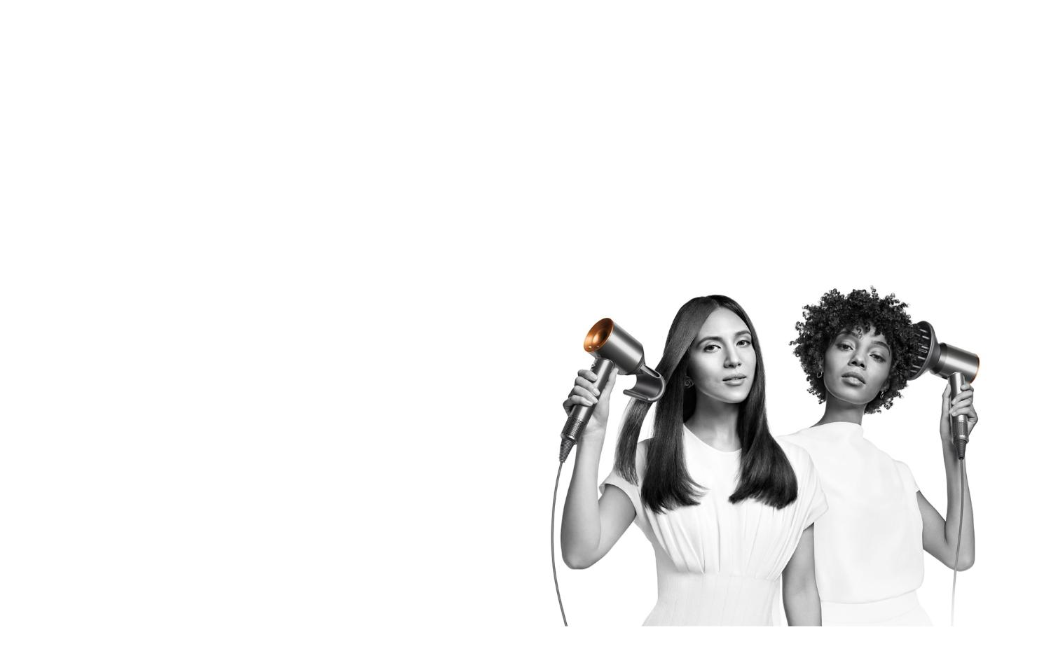 Two women dry their hair with the Dyson Supersonic hair dryer. The woman on the left uses the Flyaway attachment to smooth her straight long hair and the woman on the right uses the Diffuser attachment to shape her coily short hair.