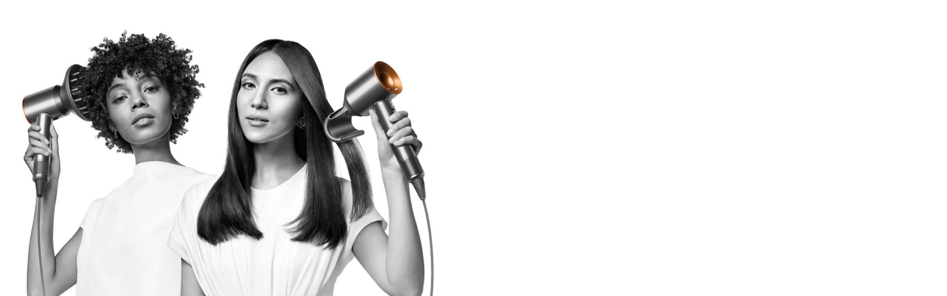 سيدتان تقومان بتجفيف شعرهما باستخدام مجفف الشعرDyson Supersonic. تَستخدم السيدة على اليسار ملحق إخفاء الشعر المتطاير لتنعيم شعرها الطويل المالس، بينما تَستخدم السيدة على اليمين ملحق مُوزِّع الهواء لتشكيل شعرها القصير الملفوف.