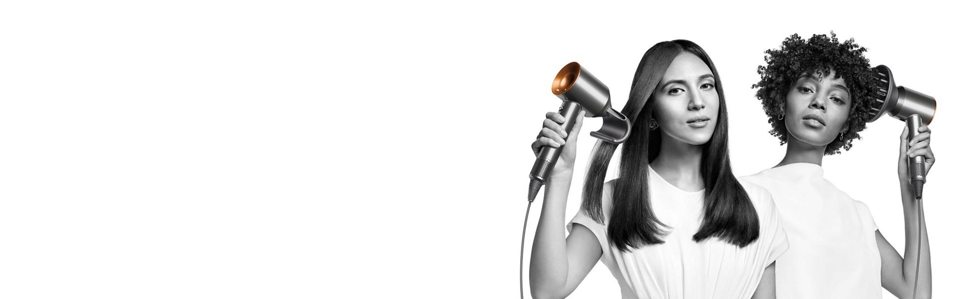 Two women dry their hair with the Dyson Supersonic hair dryer. The woman on the left uses the Flyaway attachment to smooth her straight long hair and the woman on the right uses the Diffuser attachment to shape her coily short hair.
