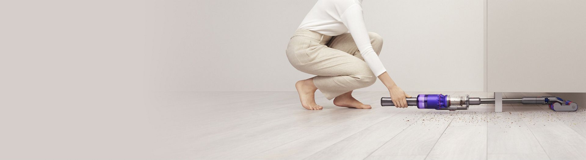 A woman vacuuming under furniture with the Dyson Omni-glide vacuum in low profile.