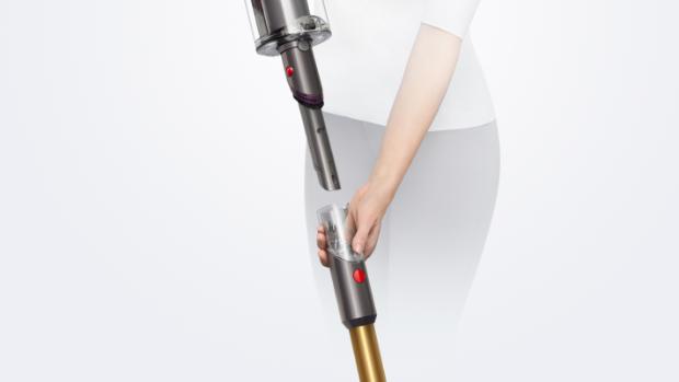 A woman removes the wand on the Dyson V15 Detect vacuum to reveal the Built-in dusting and crevice tool.