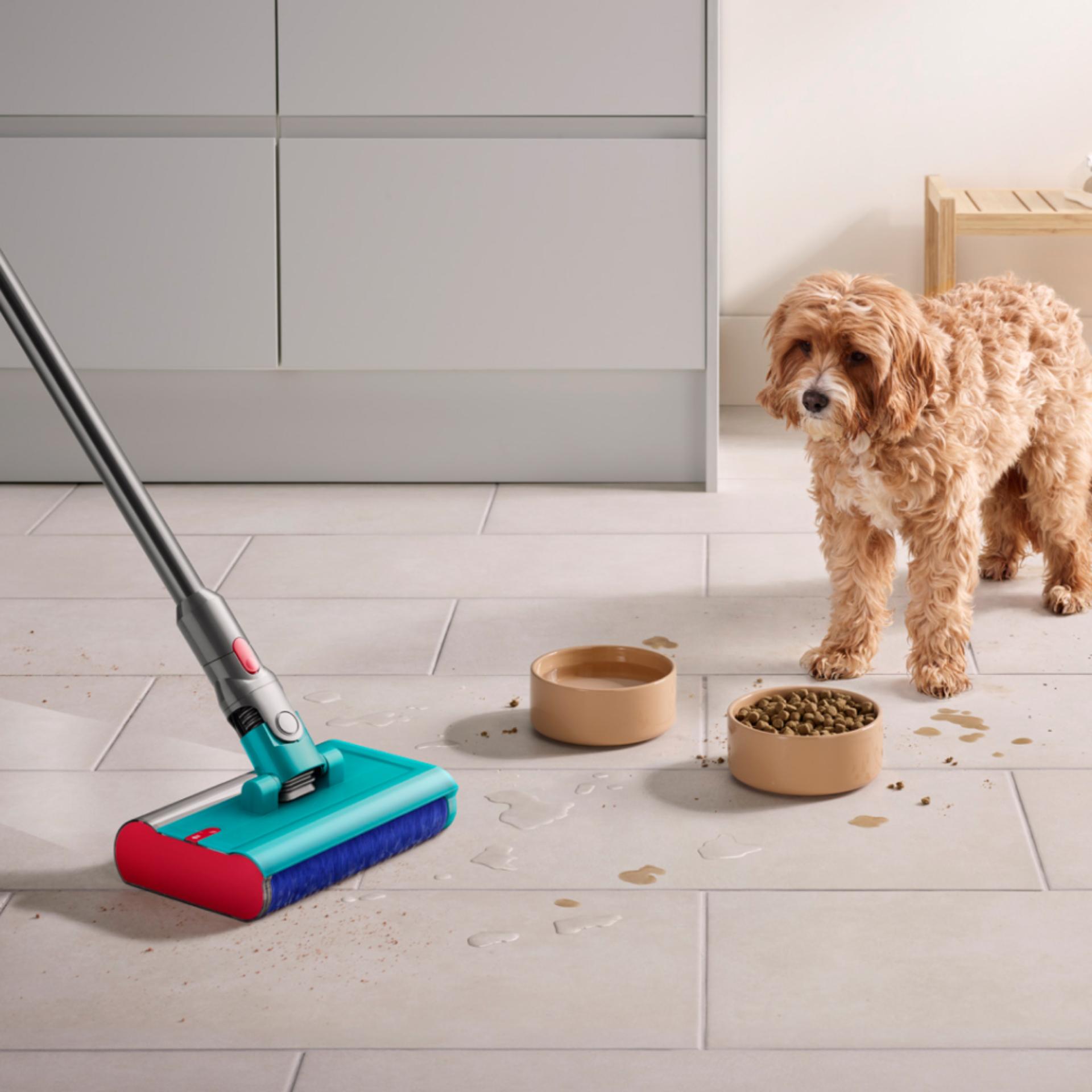 The Dyson V15s Detect Submarine cleans the floor of a kitchen with a dog and dog food bowls in the background.