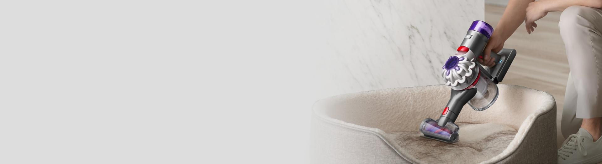 Dyson V8 handheld vacuum removing hair from a pet bed.