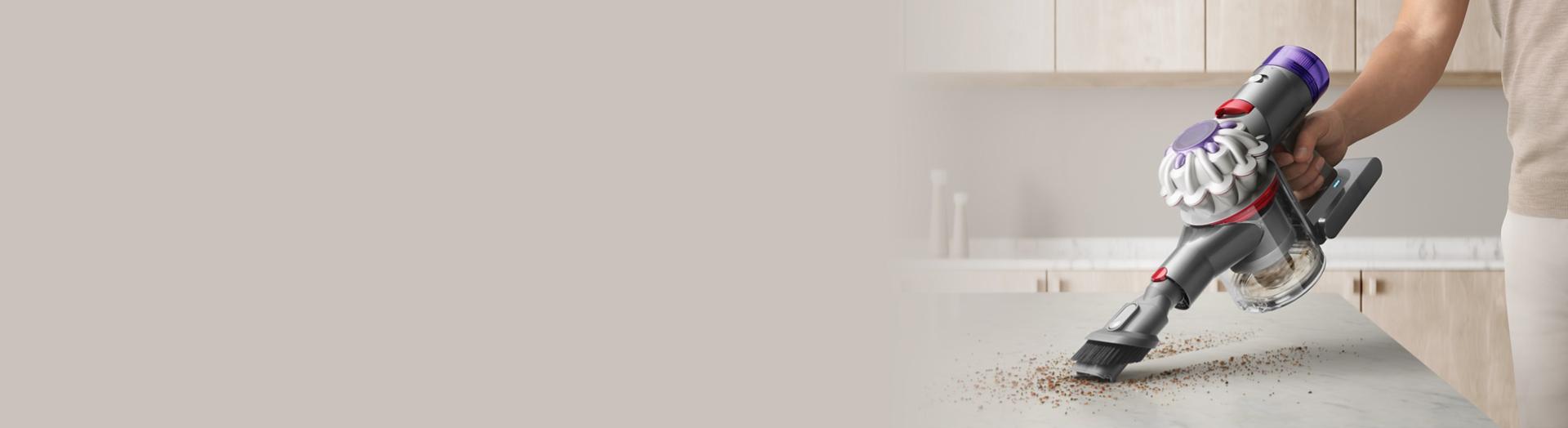 Dyson V8 handheld vacuum removing crumbs from a kitchen work surface.