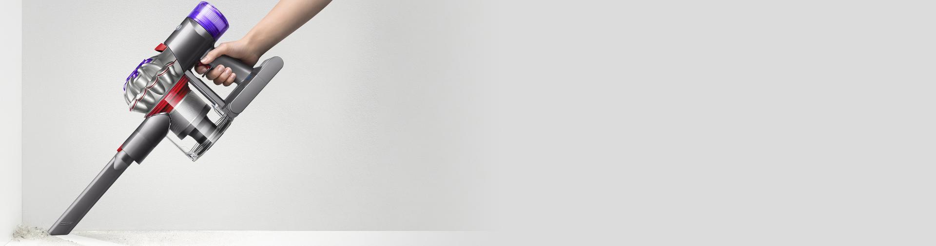 مشهد جانبي لمكنسة Dyson V87 في الوضع المحمول بينما تقوم بتنظيف أحد الأركان.