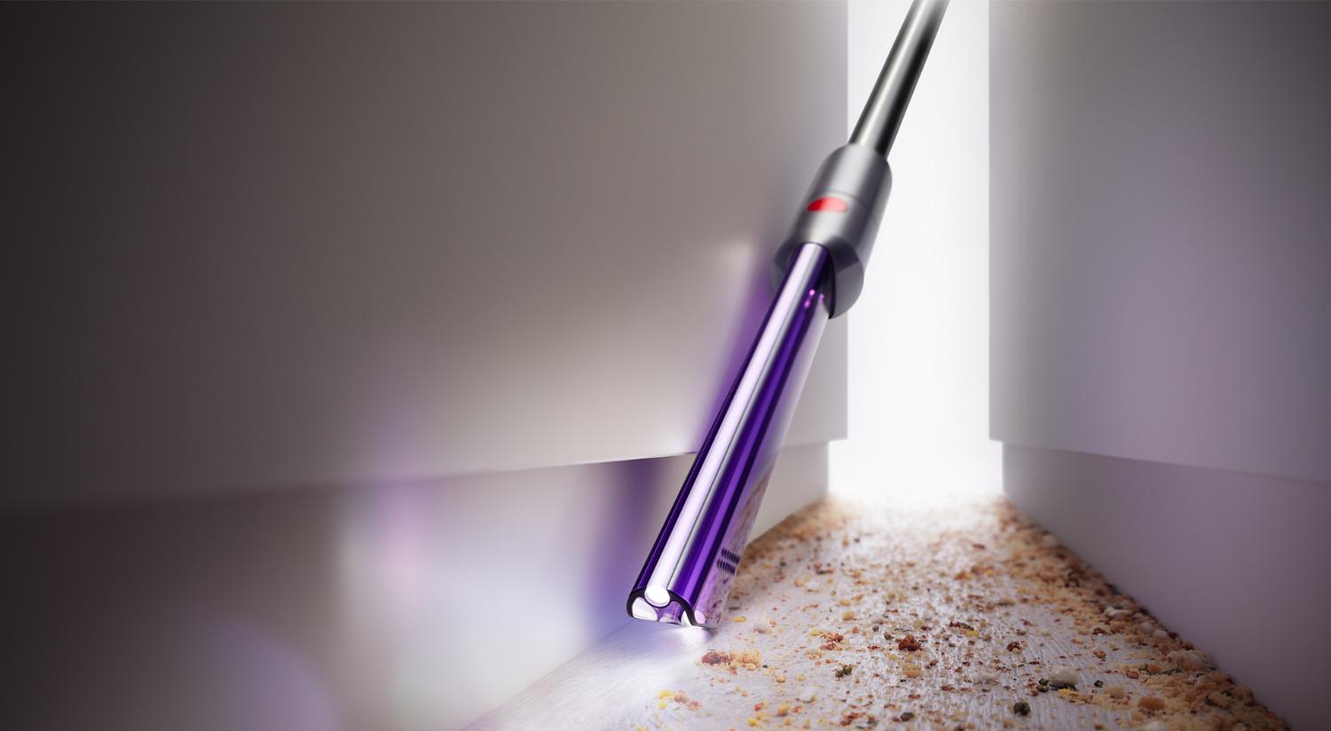 Woman using Dyson Omni-glide™ vacuum to clean under a cupboard.