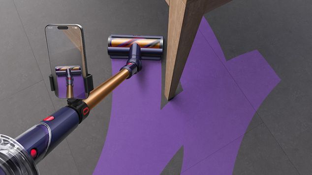 Aspirapolvere senza filo Dyson Gen5detect, con telefono e morsetto per telefono Dyson CleanTrace, mostrato mentre lascia una traccia viola sul pavimento attorno alla gamba di un tavolo