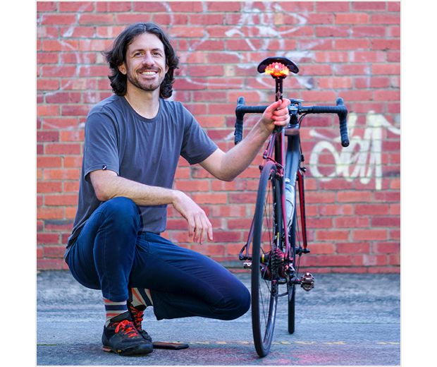 Čovjek kleči pored bicikla naslonjenog na zid od cigle